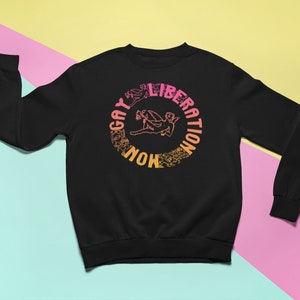 May include: Black sweatshirt with a graphic print of a winged figure in a circle with the text "NOW GAY LIBERATION" in a gradient of pink, orange, and yellow.