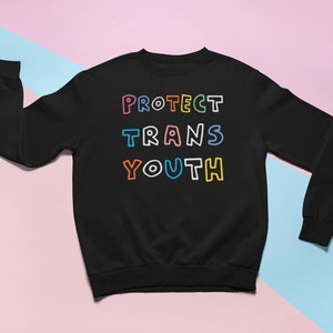 Op de afbeelding: Zwart sweatshirt met de tekst "PROTECT TRANS YOUTH" in kleurrijke omlijnde letters.