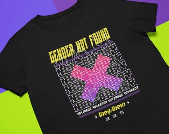 May include: Black t-shirt with a graphic design that says "Gender Not Found" with the words "Non-Binary" repeated multiple times in a stacked pattern. The graphic also includes a pink and purple X with flames. The text "404 Error 404 Error 404 Error 404 Error" is printed below the graphic. The text "they/them" is printed below the error message.