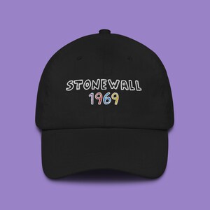 May include: A black baseball cap with the text "STONEWALL 1969" embroidered in white with colourful accents.