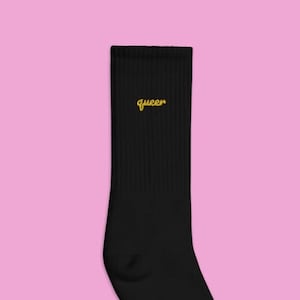 Peut inclure: Chaussettes noires montantes avec le mot "queer" brodé en jaune sur le devant.