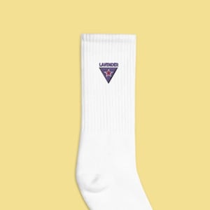 Puede incluir: Calcetines blancos hasta la pantorrilla con un logotipo triangular que dice "Lavender" en fuente morada. El logotipo tiene una estrella rosa en el centro.