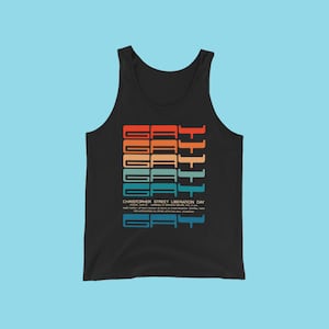 May include: Black tank top with a graphic design featuring the word "GAY" repeated in a rainbow color scheme. The text "Christopher Street Liberation Day" is printed below the graphic.
