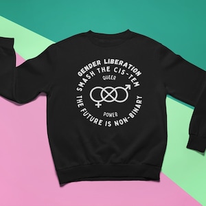 Puede incluir: Sudadera negra con un estampado gráfico blanco que dice "Gender Liberation Smash the Cis-tem Queer Power The Future is Non-Binary". El gráfico también incluye un símbolo de un símbolo femenino y masculino entrelazado.