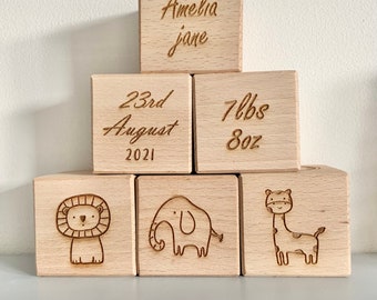 May include: Wooden blocks with engraved details for a baby's birth. The blocks read "Amelia Jane", "23rd August 2021", "7lbs 8oz", and feature a lion, elephant, and giraffe.