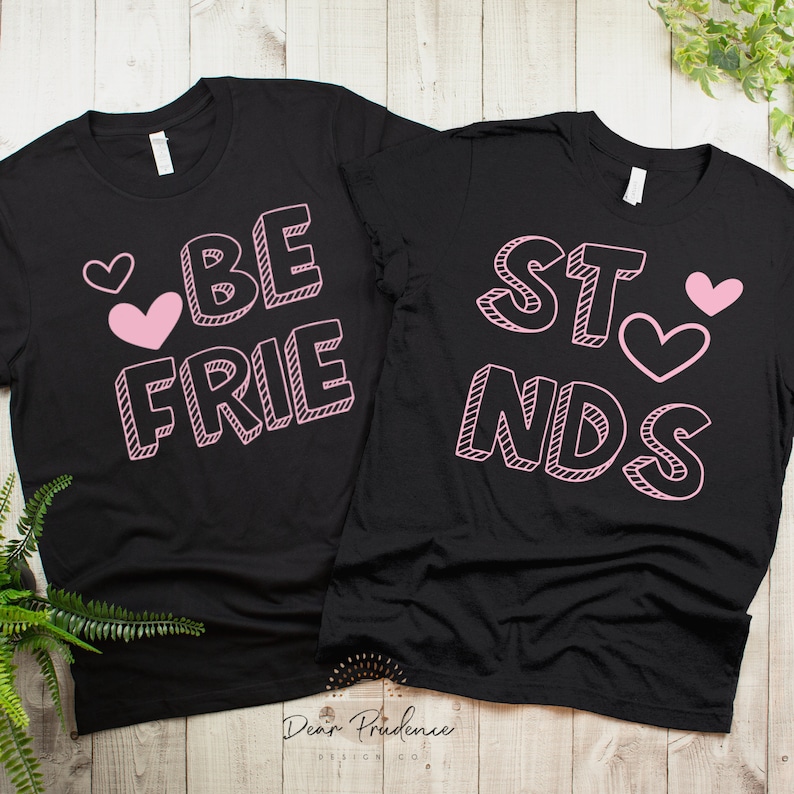 May include: Two black t-shirts with pink text and hearts. One shirt says "BE FRIENDS" and the other says "BEST" with a heart.