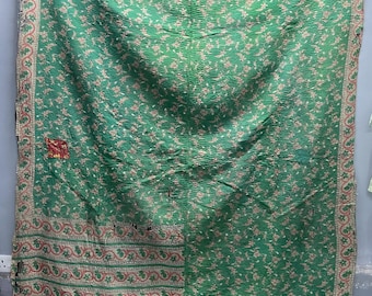 Op de afbeelding: Een rechthoekige groene kantha-quilt met een herhalend bloemenpatroon in lichtbeige. Het textiel heeft een zichtbare rijgsteektextuur, een decoratieve rand met rode en beige krulmotieven en een kleine rode lap aan de linkerzijde.