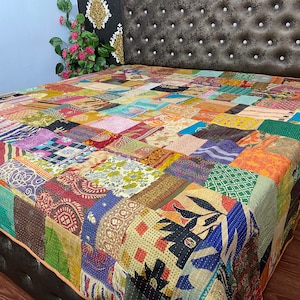May include: A colorful patchwork quilt made from repurposed fabrics. The quilt is made up of squares of different colors and patterns, including floral, paisley, and geometric designs. The quilt is laid out on a bed with a dark headboard.