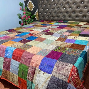 May include: A colorful patchwork quilt made from repurposed silk fabric. The quilt is made up of squares of different colors and patterns, including floral, paisley, and geometric designs. The quilt is perfect for adding a touch of bohemian style to any bedroom.