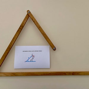 May include: A wooden triangle tool with a white card attached to it. The card has a diagram of a triangle with the text "ONE EXAMPLE IS ANGLE A ACUTE, IMPOSSIBLE TRIANGLE".