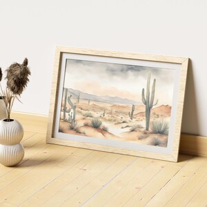 Laid gently on an oak-textured floor, the beautiful watercolor desert landscape piece rests beside a decorative plastic vase adorned with ornamental feathers