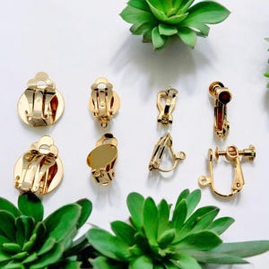 May include: A set of eight gold-toned earring clips for crafting jewelry. The clips are in various styles, including round, oval, and screw-back.