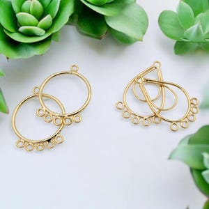 May include: Two pairs of gold-toned earring findings with multiple jump rings. One pair is a round hoop with five jump rings and the other pair is a teardrop shape with five jump rings.