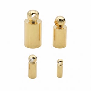 May include: Four gold-toned cylindrical jewelry findings arranged in a descending size order. Each piece features a smooth, polished finish and a spherical top component with a small, circular hole centered at the top for threading or attachment.