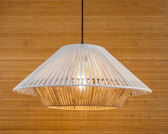 Op de afbeelding: Een witte touw hanglamp met een geweven kap hangt aan een zwart snoer tegen een achtergrond van houten panelen.