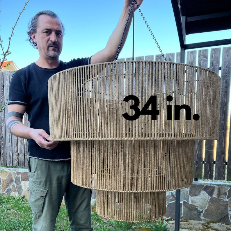 May include: A three-tiered cylindrical pendant light fixture wrapped in natural tan jute rope. The structure features a wide top tier, a medium middle tier, and a smaller bottom tier, all suspended by black chains. The text 34 in. is visible.