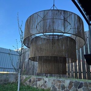 May include: A three-tiered drum chandelier featuring a brown rope-wrapped frame. The fixture consists of three concentric circular rings of varying diameters, each covered in vertical strands of brown cord, suspended by a central metal chain.