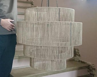 May include: A three-tiered drum chandelier featuring a light beige rope-wrapped frame. The fixture is suspended by thin black chains connected to a central black canopy, creating a layered cylindrical silhouette with a natural fiber texture.