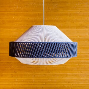May include: A white and blue woven pendant light fixture hangs from the ceiling against a wood panel background.