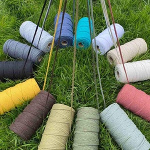 May include: A collection of fourteen cylindrical spools of cord in various colors including black, yellow, brown, tan, olive green, light blue, pink, white, cream, grey, dark blue, and turquoise, each with a single strand extending upward.