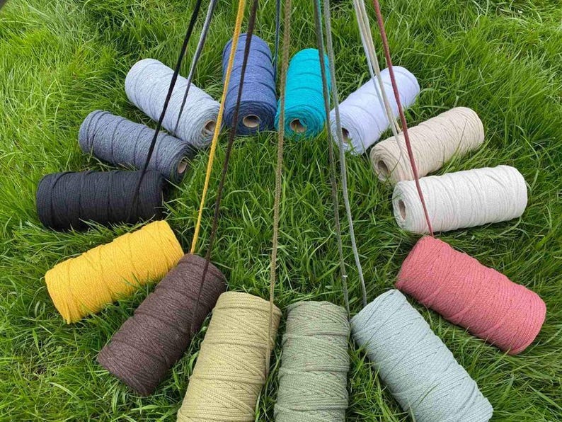 May include: A collection of fourteen cylindrical spools of cord in various colors including black, yellow, brown, tan, olive green, light blue, pink, white, cream, grey, dark blue, and turquoise, each with a single strand extending upward.