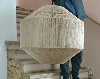 May include: A large, drum-shaped pendant light fixture featuring a beige, natural-colored string or twine wrapping that covers the entire exterior surface, creating a textured, vertical line pattern around the cylindrical frame.