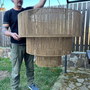 May include: A three-tiered cylindrical pendant light fixture constructed from a metal frame wrapped in natural tan jute twine. The fixture features three concentric circular tiers of varying diameters, suspended by a thin black metal chain.