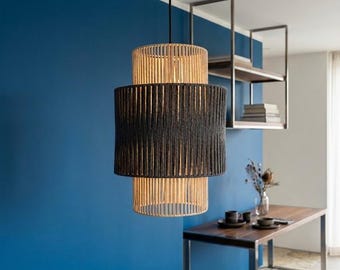 May include: A cylindrical pendant light fixture featuring a layered design with a central band of dark charcoal gray vertical cord wrapping, flanked by top and bottom sections of natural light beige vertical cord wrapping, suspended by a black cord.