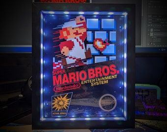 May include: A framed Super Mario Bros. Entertainment System artwork. The artwork features the game's logo and pixelated Mario character. The frame is black with blue LED lights around the inside edge. The Nintendo logo is visible.