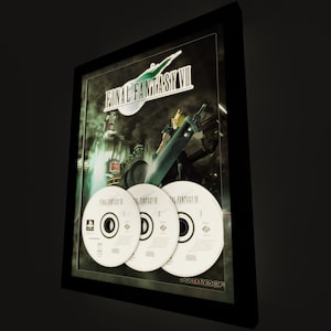 May include: Framed Final Fantasy VII artwork featuring the game's logo, a character with a large sword, and three game discs. The artwork is in a black frame, with the SquareSoft logo visible.