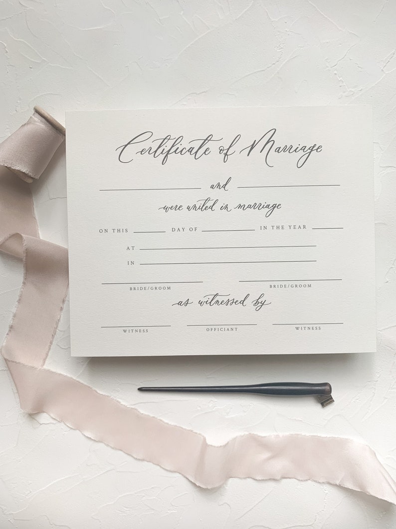May include: A blank white certificate of marriage with the text "Certificate of Marriage" and "as witnessed by" in cursive script. The certificate has lines for the bride and groom's names, the date, and the officiant's name.