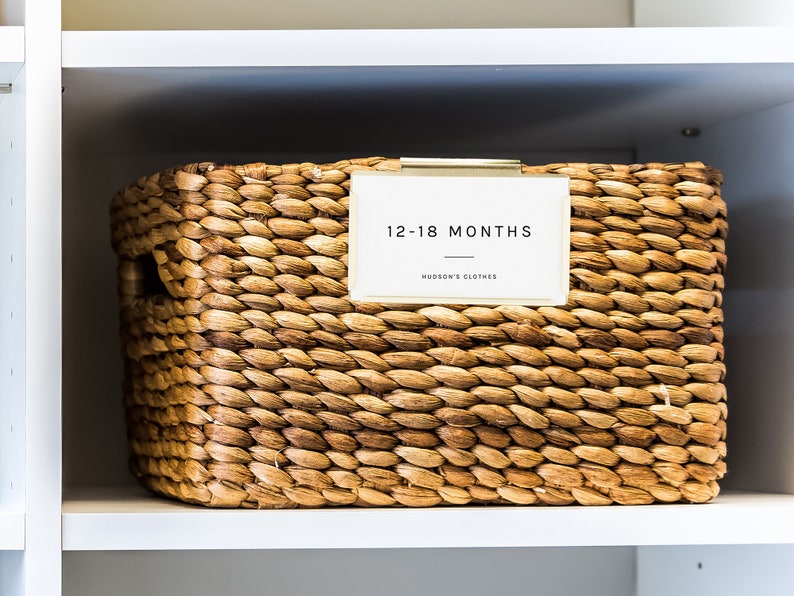May include: A woven wicker basket with a label that reads "12-18 Months Hudson's Clothes".