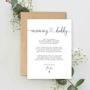 May include: A white card with black text that reads "mummy daddy" with a heart symbol between the words. The card has a message about a new baby and the love between a parent and child. The card is on a brown envelope with green leaves.