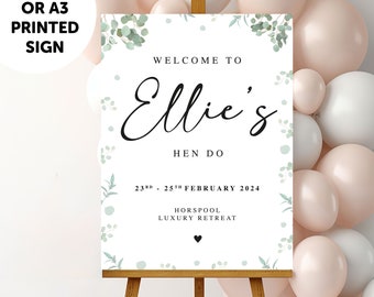 May include: A white rectangular sign on a wooden easel featuring green eucalyptus leaf illustrations. The text reads: WELCOME TO Ellie's HEN DO 23RD - 25TH FEBRUARY 2024 HORSPOOL LUXURY RETREAT. A small black heart is centered at the bottom.