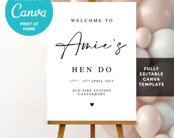May include: A white rectangular welcome sign on a wooden easel featuring black text that reads Welcome to Amie's Hen Do, 17th - 19th April 2025, Old Fire Station Canterbury, with a small black heart icon at the bottom center.