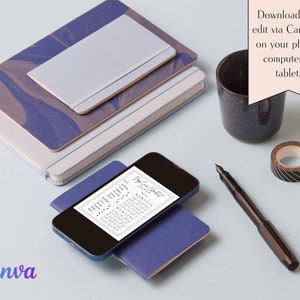 May include: A black and white printable planner page with the text "Day Planner" on a smartphone screen. The phone is on top of a blue notebook. There is a black and white roll of tape, a black fountain pen, and a stack of notebooks with blue and gray marbled covers on a light blue surface.