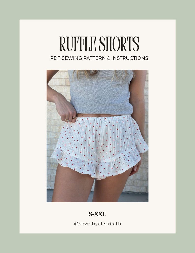 Op de afbeelding: Witte ruffle shorts met een rood hartjespatroon. De shorts hebben een gefranjerde zoom en maken deel uit van een PDF naaipatroon. De tekst "RUFFLE SHORTS" en "PDF SEWING PATTERN & INSTRUCTIONS" wordt weergegeven.