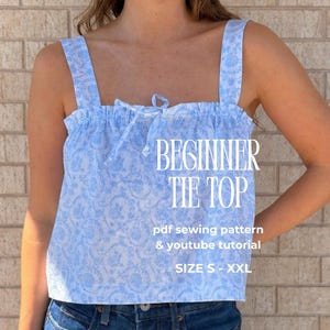 May include: A light blue tie top with a white floral pattern. The top has wide straps and a gathered neckline with a tie detail. Text on the image reads "BEGINNER TIE TOP" and "SIZE S - XXL".