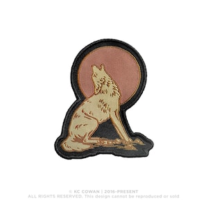 May include: Embroidered patch featuring a howling wolf silhouette in tan and brown against a peach-colored moon. The patch has a black border and is likely for clothing or accessories. The design includes the text "KC COWAN | 2016-PRESENT".