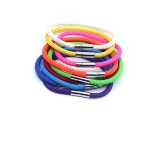 May include: A stack of colorful, adjustable, rope bracelets with silver metal clasps. The bracelets are in the following order from top to bottom: white, yellow, pink, orange, green, blue, and purple.