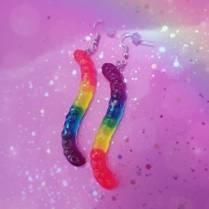 May include: Rainbow gummy worm dangle earrings with silver hooks. The gummy worms are translucent and have glitter embedded in them.