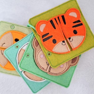 Puede incluir: Una pila de coloridos rompecabezas de animales de fieltro. Los rompecabezas presentan un tigre, un mono y un perro, cada uno con un diseño de dos piezas. Los cuadrados de fieltro son en tonos de verde, azul y naranja, con las caras de los animales en marrón y naranja.