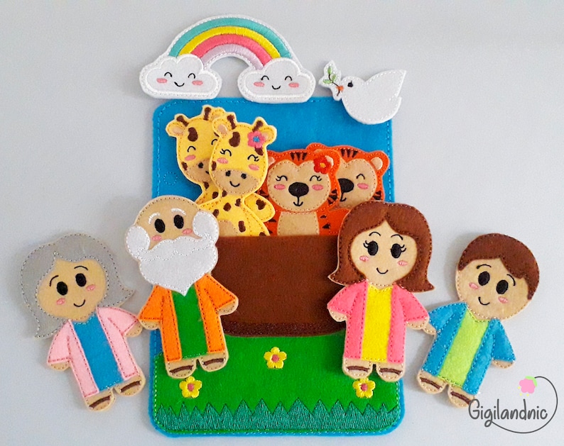 Pode incluir: Marionetes de dedo de feltro de um homem com barba, uma mulher com cabelo grisalho, um menino, uma menina, duas girafas e dois tigres. As marionetes est&atilde;o dispostas em frente a um fundo de feltro azul com um arco-&iacute;ris e uma pomba branca. O fundo tamb&eacute;m tem um bolso de feltro marrom com grama verde e flores amarelas.