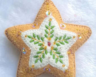 May include: A felt star-shaped ornament with a gingerbread cookie design. The star is decorated with green and gold embroidery, white beads, and iridescent sequins.