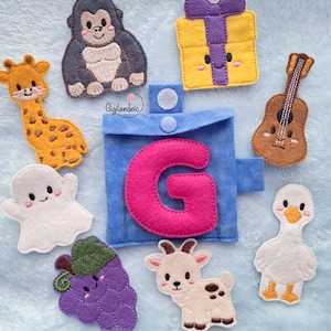 May include: A blue felt pouch with a pink letter G, surrounded by felt shapes including a giraffe, gorilla, gift box, guitar, ghost, grapes, goat, and goose. The pouch features a snap closure and the text Gigilandnic is printed above it.