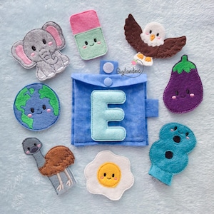 May include: A blue felt pouch with a light blue letter E on the front, surrounded by felt shapes including a gray elephant, a pink and green eraser, a brown eagle, a purple eggplant, a blue earth, an emu, a fried egg, and a blue number eight.