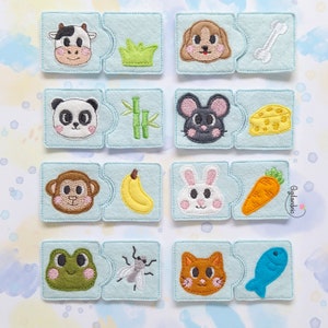 May include: A set of 10 felt puzzle pieces featuring animal and food pairings. Each puzzle piece is blue with white stitching around the edges. The animals include a cow, dog, panda, mouse, monkey, rabbit, frog, cat, and a fly. The food items include grass, bone, bamboo, cheese, banana, carrot, fly, fish.