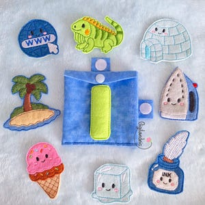 May include: A blue felt pouch with a lime green letter I, surrounded by embroidered felt patches including a globe with WWW, a green iguana, an igloo, a palm tree on an island, an ice cream cone, an ice cube, an iron, and an ink pot with a quill.