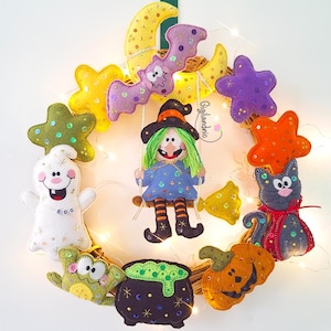 May include: A handmade Halloween wreath featuring felt decorations. The wreath includes a witch on a swing, a ghost, a cat, a pumpkin, a cauldron, stars, a bat, and a moon. The wreath is decorated with fairy lights and the text "Gigilandrio".