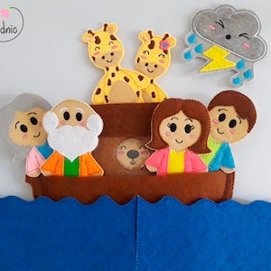 Pode incluir: Um conjunto de fantoches de dedo de feltro com a fam&iacute;lia de No&eacute; e duas girafas. Os fantoches est&atilde;o em uma arca de feltro marrom com um oceano de feltro azul abaixo. Uma nuvem cinza de feltro com um raio amarelo e gotas de chuva est&aacute; no canto superior direito.
